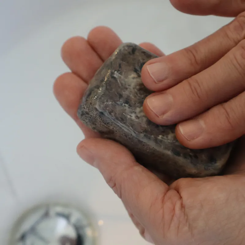 hands rinsing pine tar soap bar under water