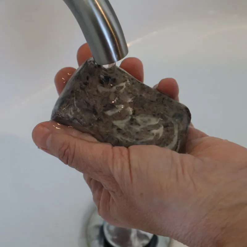 hands holding pine tar soap under running water
