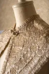 Detail of the collar of a cream-coloured embroidered child's cape.