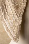 Detail of the lower front left corner of a cream-coloured embroidered child's cape displayed on a dress form.