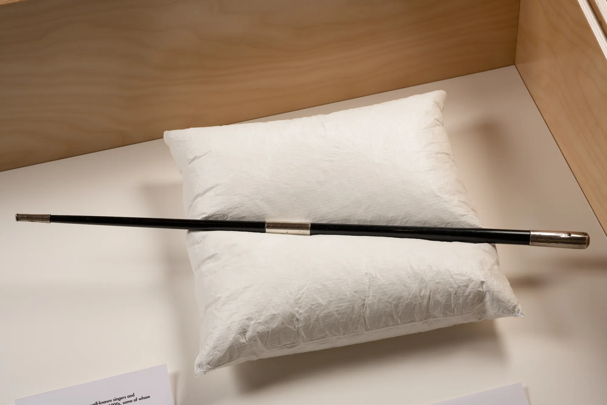 A black conductor's baton with silver ends displayed on a white cushion