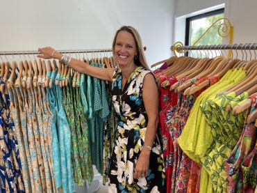 Alethea smiling between two clothes racks of colourful dresses in the Mr Peacock store