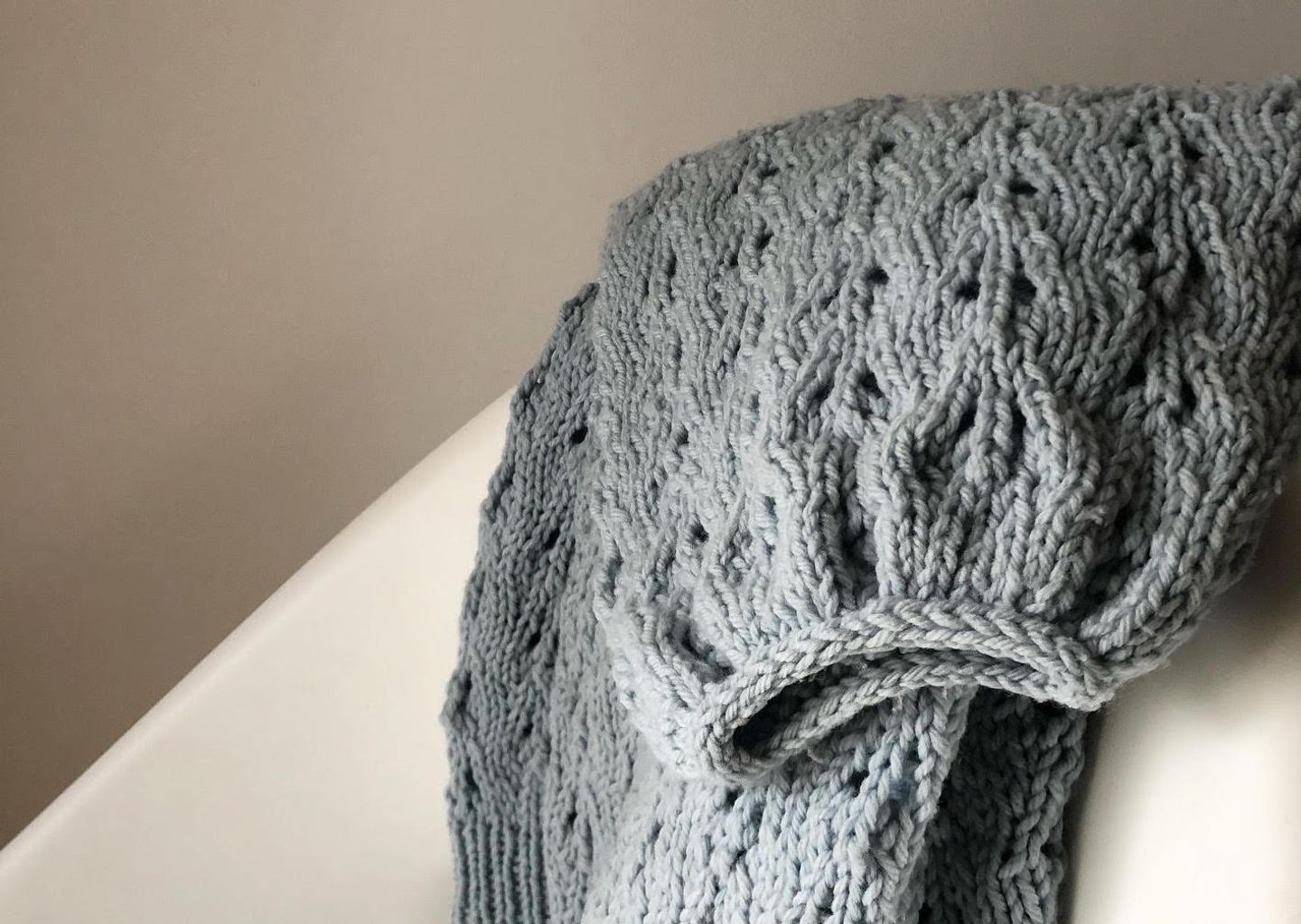 Pale blue sweater draped over a chair. It shows the cuff of a sweater which has been bound off using icrod