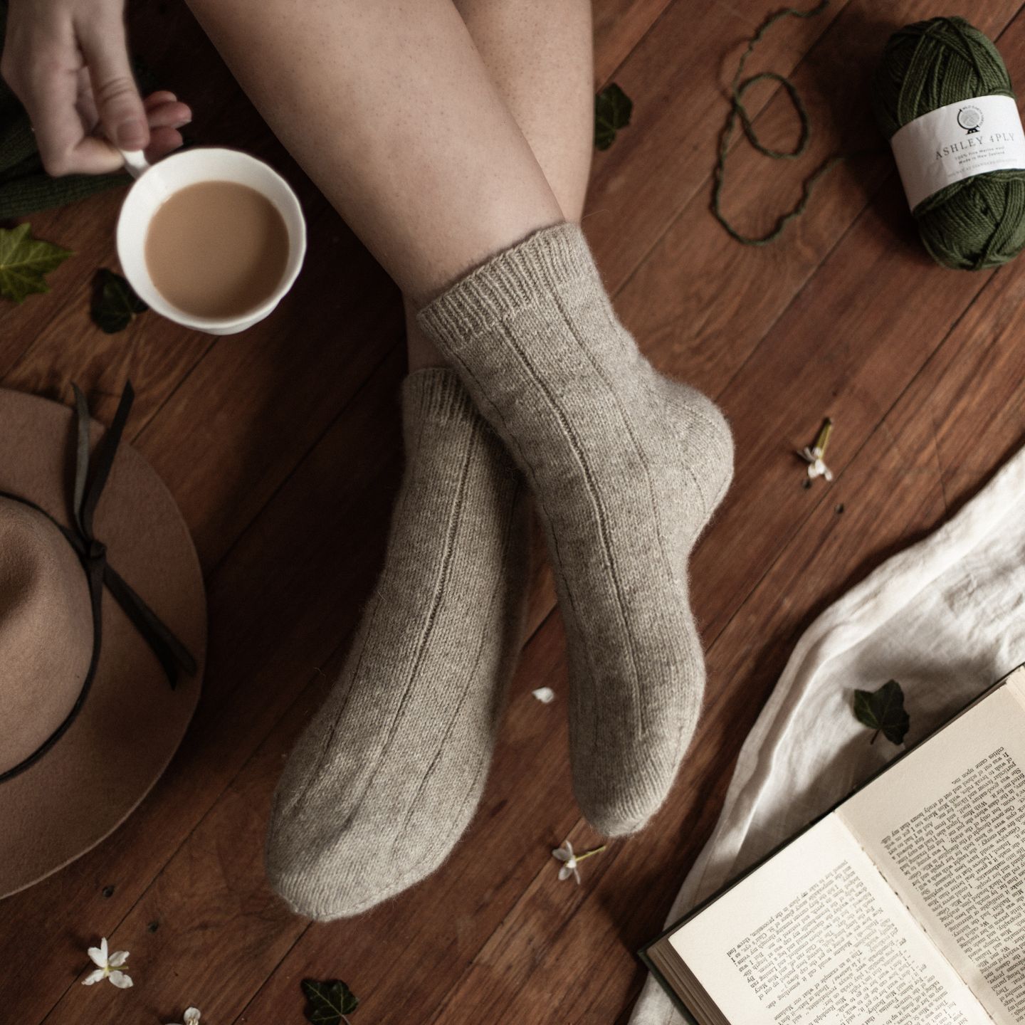 Wearing handknit socks with legs crossed on a wooden floor. Holding a cup of tea.