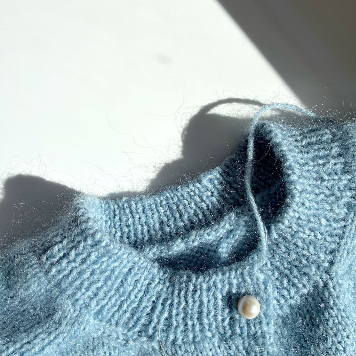 A blue mohair and merino cardigan on a white surface