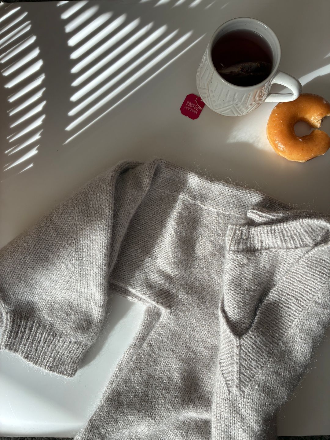 The Ridgeline Sweater beside a cup of tea and donut with a bite taken out of it because it was delicious and I couldn't wait any longer to eat it