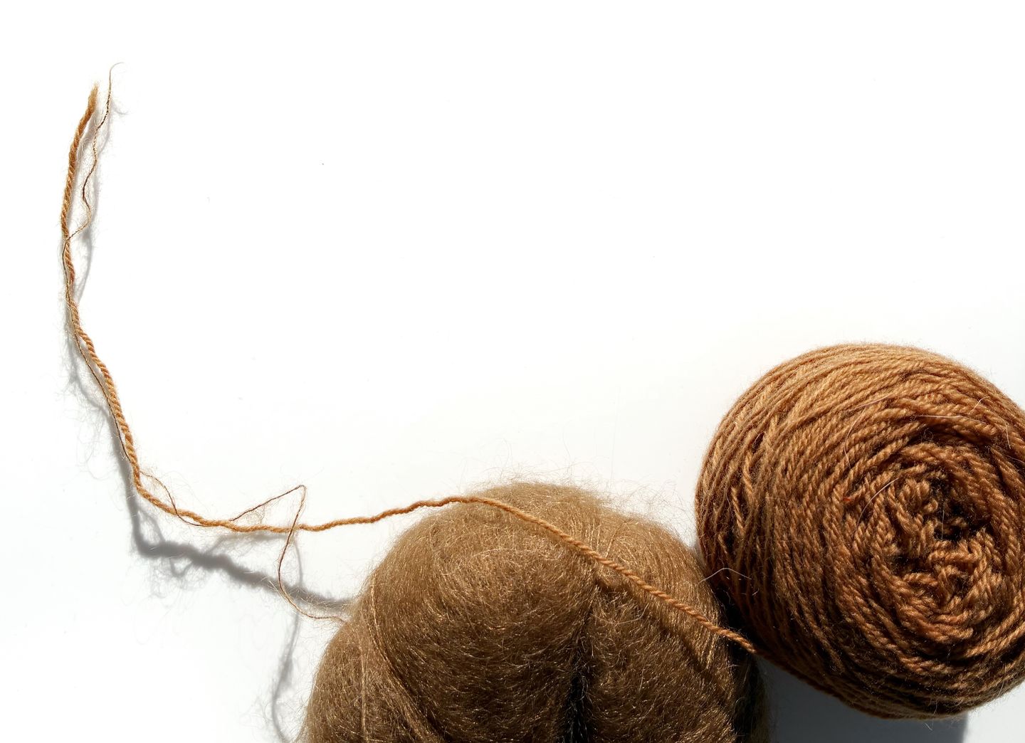 A flatlay of toffee coloured merino yarn beside mohair yarn in the same colour