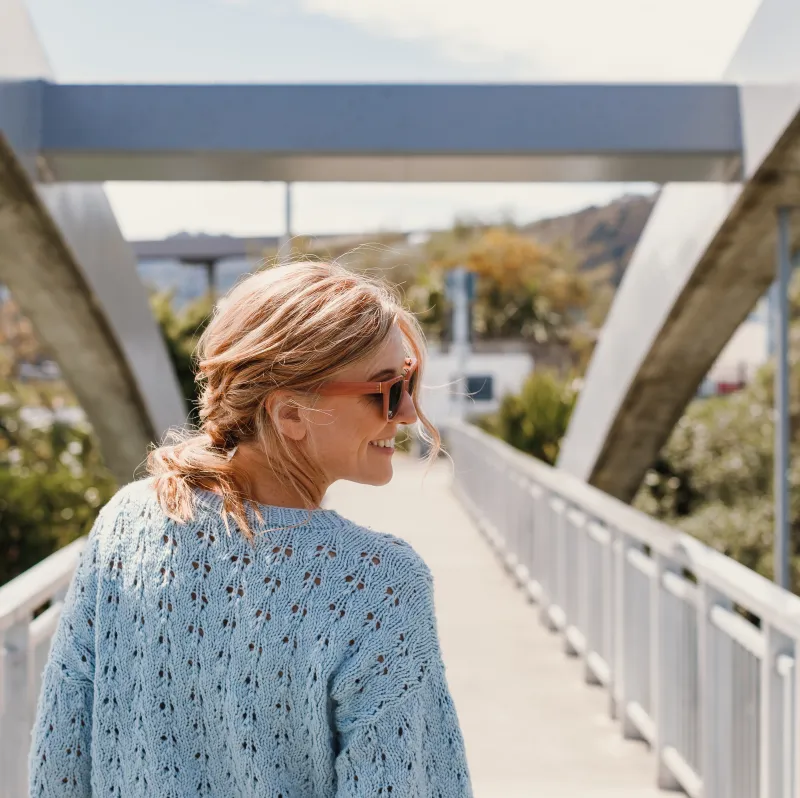 A woman on a bridge with her back to the camera. She's looking over her right shoulder and wearing a lacy, blue sweater.