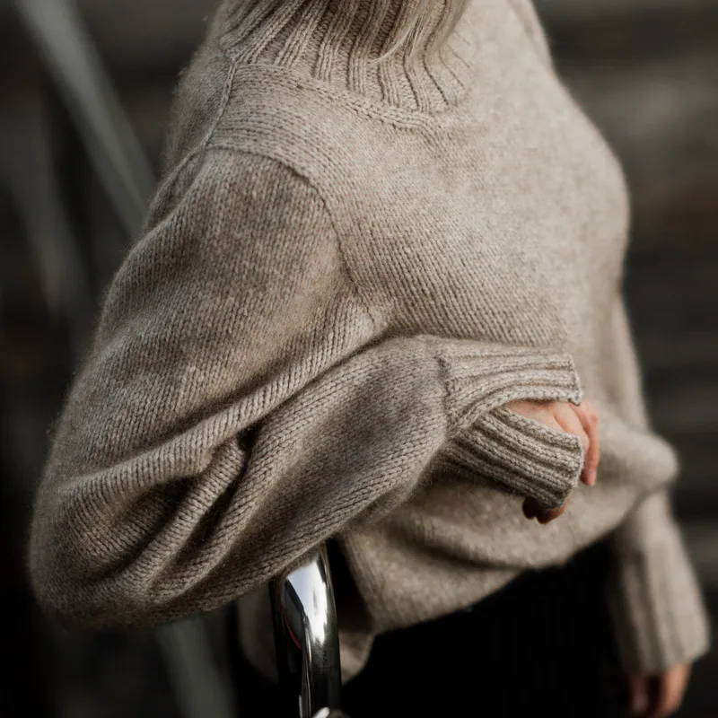 A woman wears a sweater with an elbow resting on a metal stair railing