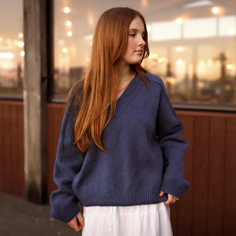 A woman looks to the right while wearing a navy blue sweater and a tiered white skirt.