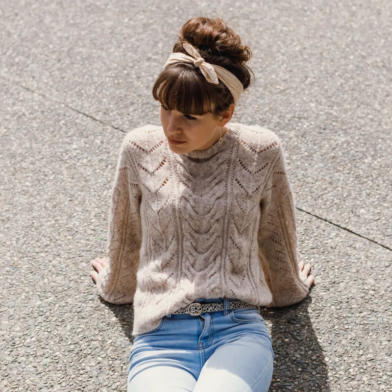 Woman sitting on the ground wearing a hand knit cable sweater