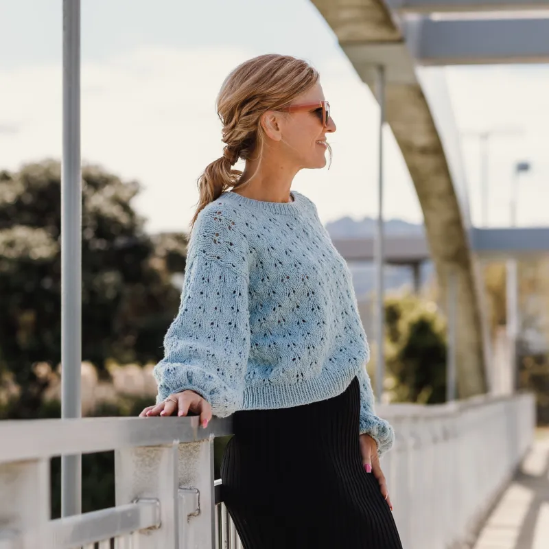 Woman standing on a bridge wearing a blue hand knit sweater