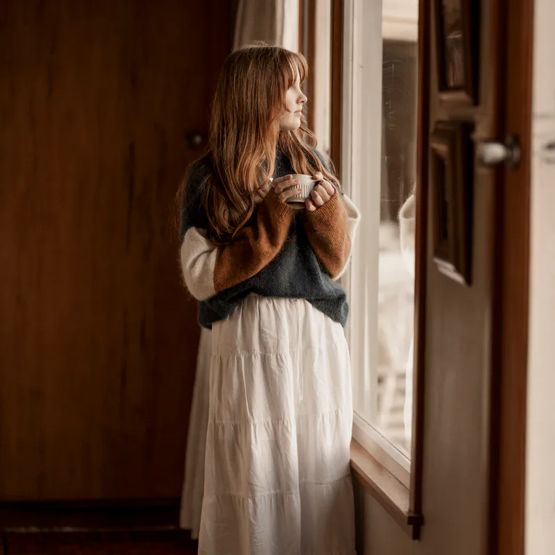 A woman looking out a window while holding a mug.