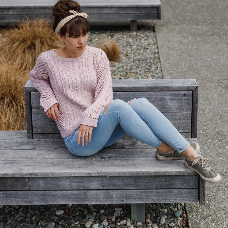 Woman sitting on a bench wearing a pink hand knit sweater