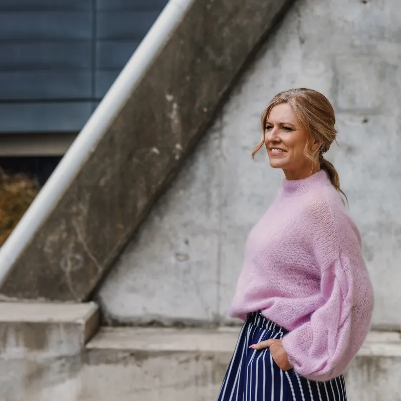 A woman wearing a fluffy pink sweater with a blue and white striped skirt. The sweater has beautiful drape and a turtleneck neckline.