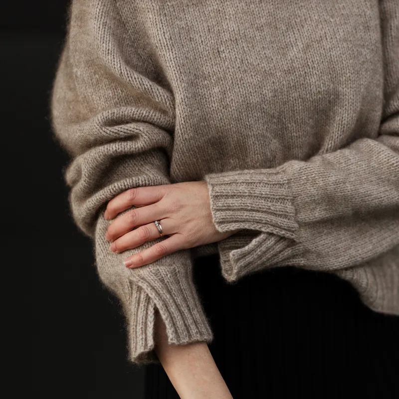 A tightly cropped photo of a woman wearing a sweater with split cuffs. Her hand rests on the forearm of the other arm, slightly lifting the sleeve as she does so.