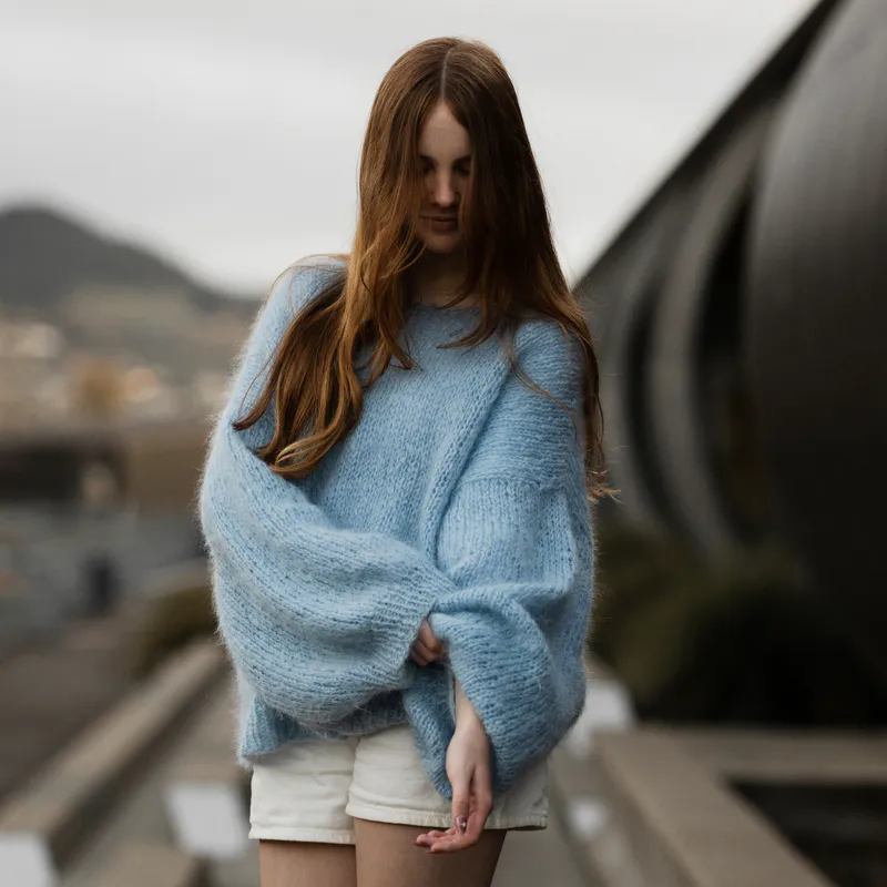 A woman wearing a blue mohair sweater. She is pulling the oversized sleeve up the right arm slightly.