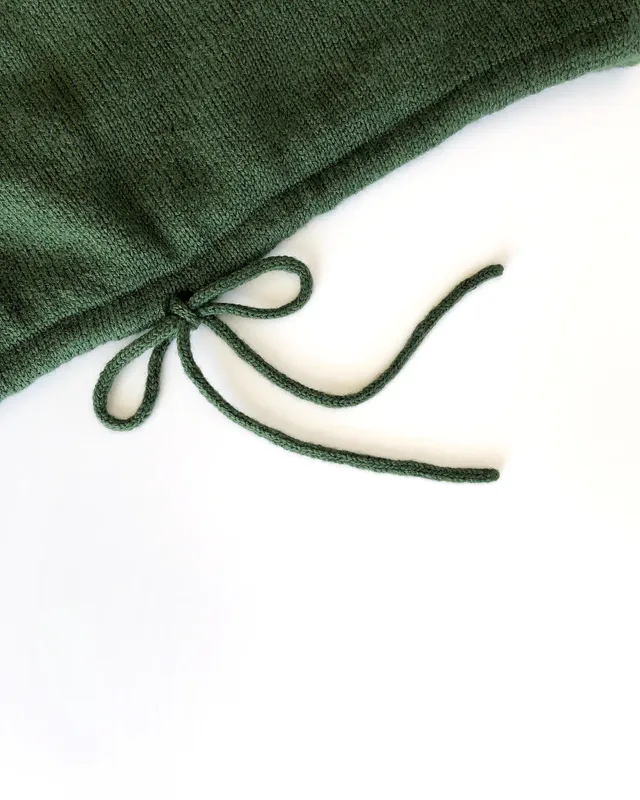 An icord hem of a green, hand knit sweater. The cord is tied in a cute bow.