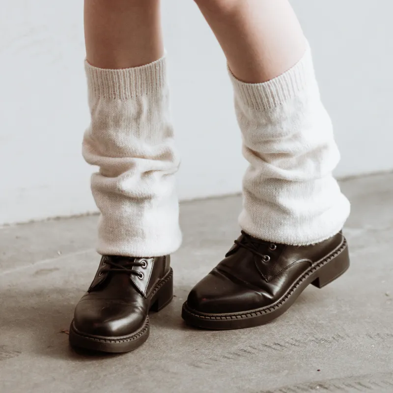 Cream coloured, slouchy leg warmers in plain knitted fabric. The front leg is bent to reveal the foot at the back.