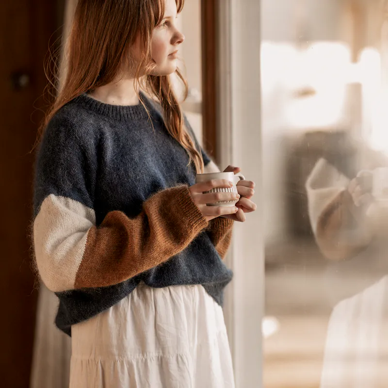 A woman looking out a window while holding a mug
