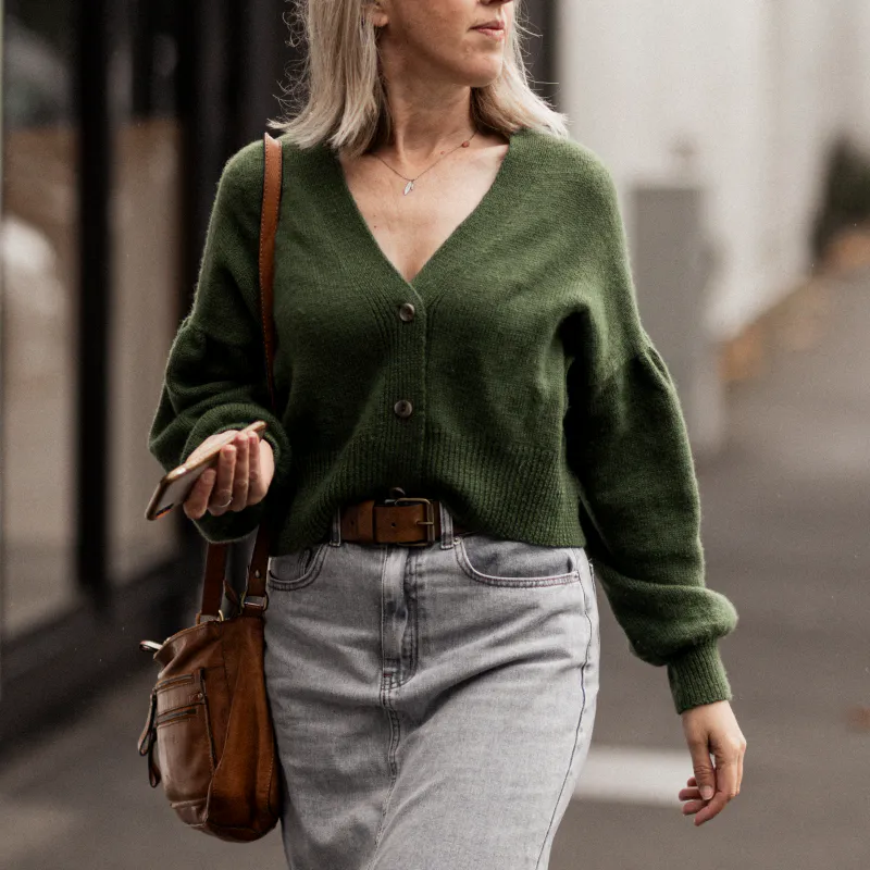 Cropped image of a woman wearing a green, hand-knit cardigan. It was made using NZ merino yarn.