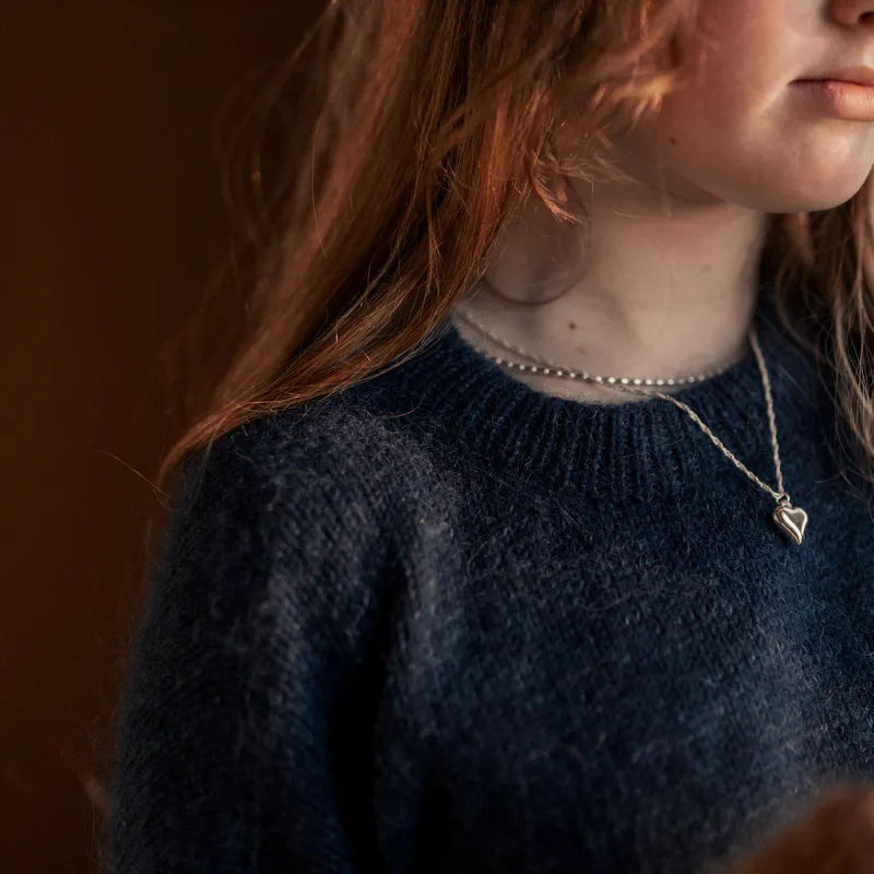 A close up of the neckline of a hand knit sweater. It's been knit in ribbing and then folded in half and sewn to the inside.