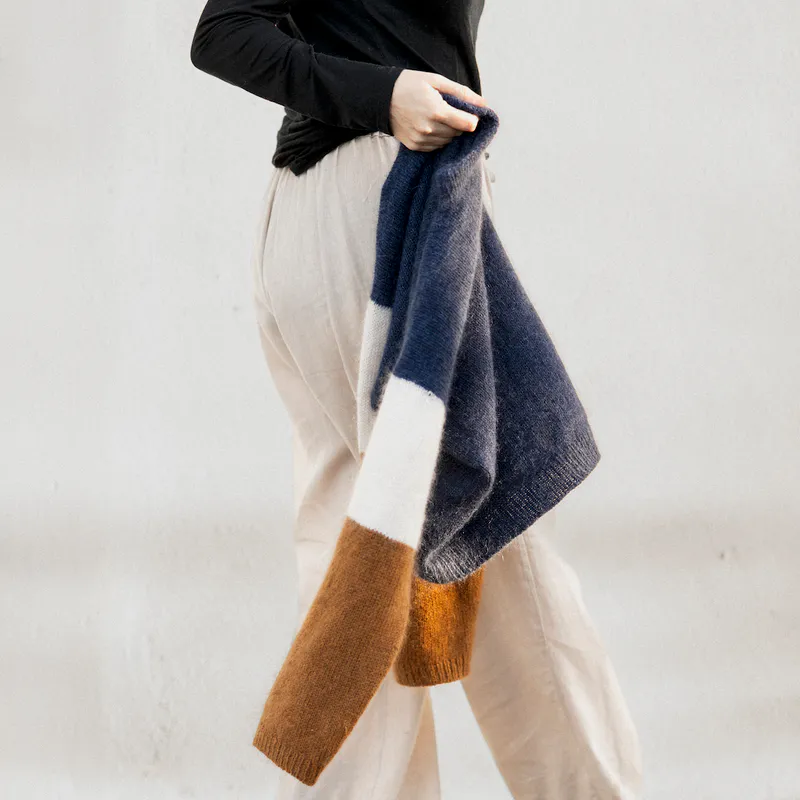 Someone holding a hand knit sweater as they walk past the camera. The sweater hangs from their hands by the collar