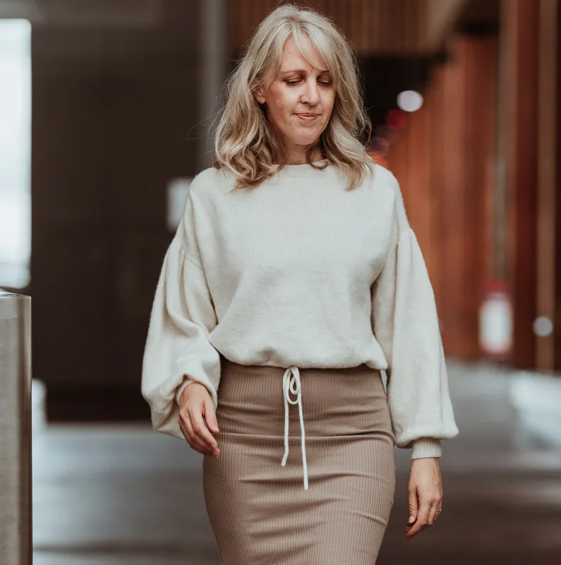 Woman looking at the ground while walking down a retail alleyway. She is wearing a cream coloured hand knit sweater.