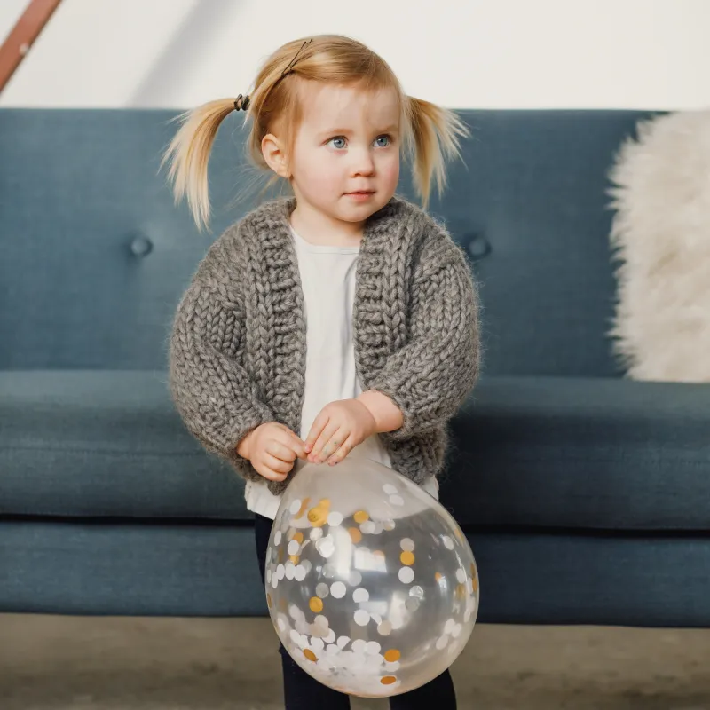 Toddler holding a balloon with confetti inside and wearing a hand knitted cardigan