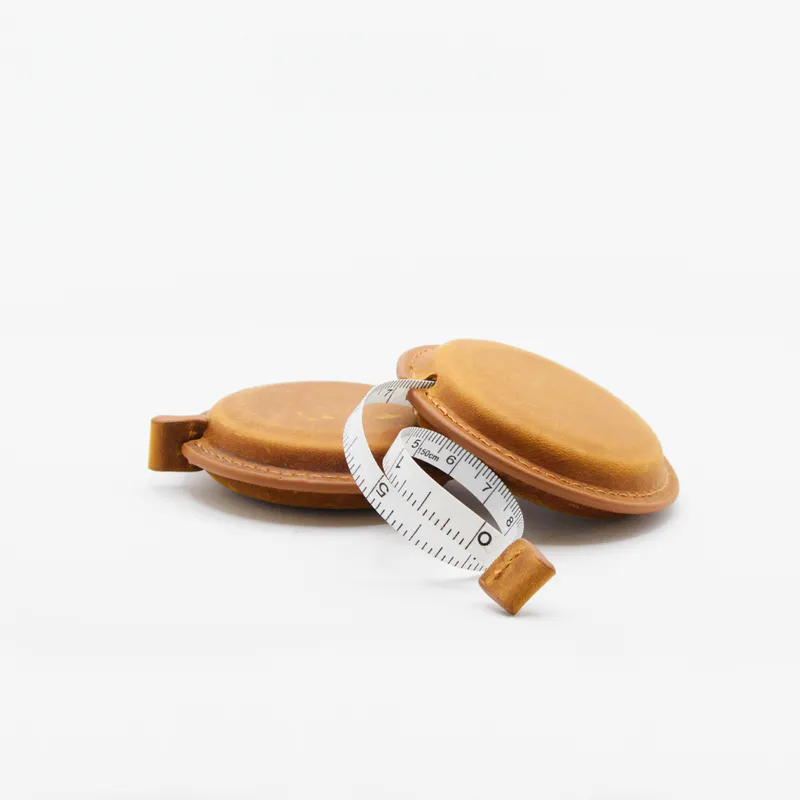 Circle shaped tape measure with leather binding. Features both imperial and metric measurements.