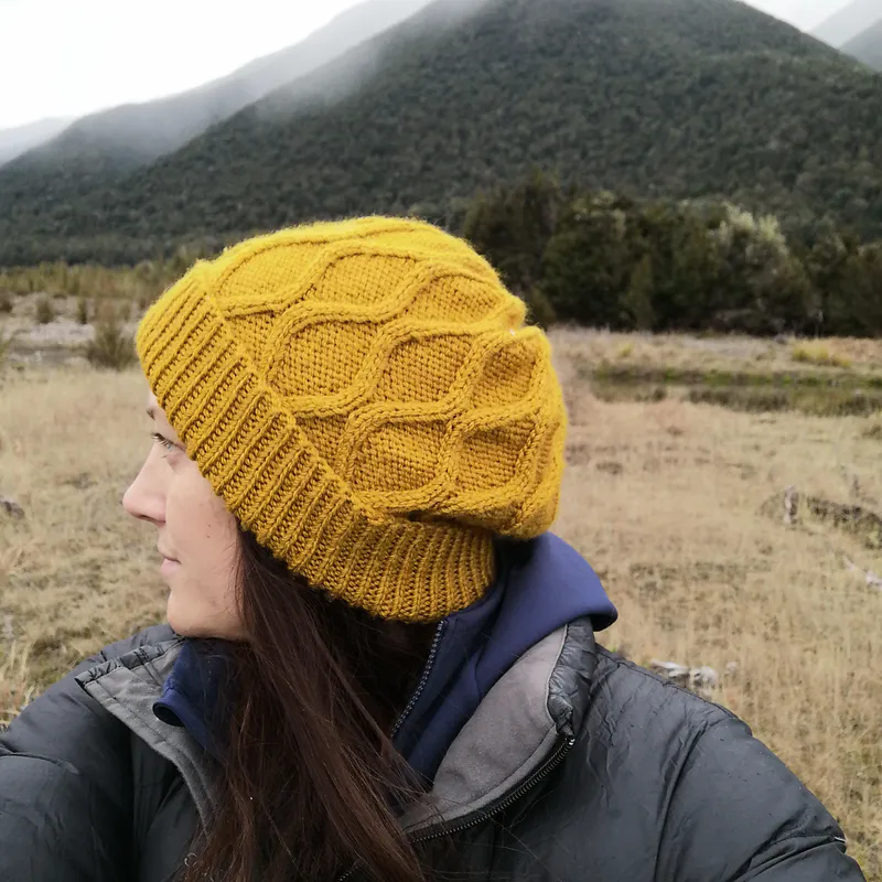 A mustard coloured Wavy Cable Hat by Toni Kroupa with NZ mountains in the background