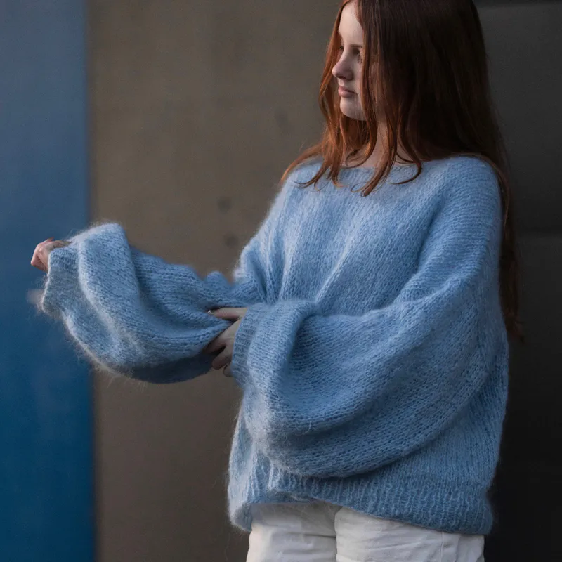 A woman wearing a blue hand-knit sweater in 12 ply mohair yarn with a loose gauge. The sleeves are huge.