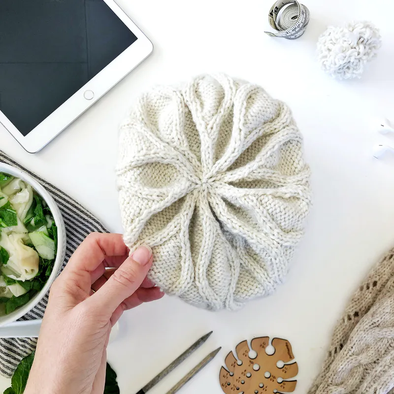 Snowflake detail on the crown of a cream coloured, hand knit hat. It was made using a PDF knitting pattern called Wavy Cable Hat.