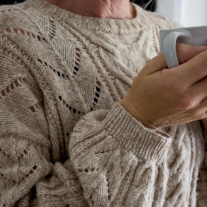 Cable Bay Sweater knitting pattern up close with a cup of coffee in one hand