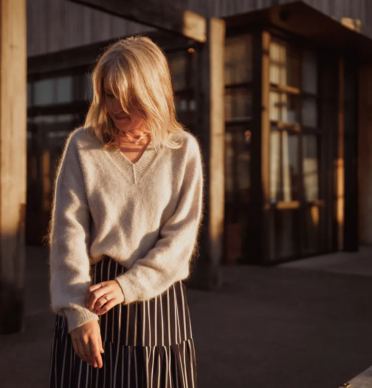 A woman looks down at the cuff of her hand knit sweater. She spent many hours knitting it but she's the warmest person in her group of friends this winter and no-one jokes about her grandma hobby now.