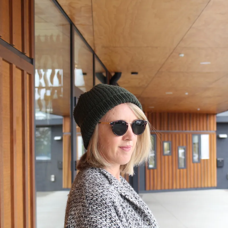 A woman stands facing to the right. She is wearing a green, hand knit beanie.