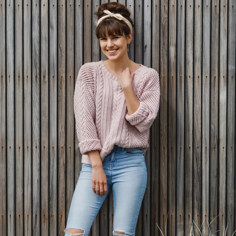 Woman wearing a pink hand knit sweater with mesh and cable stitches