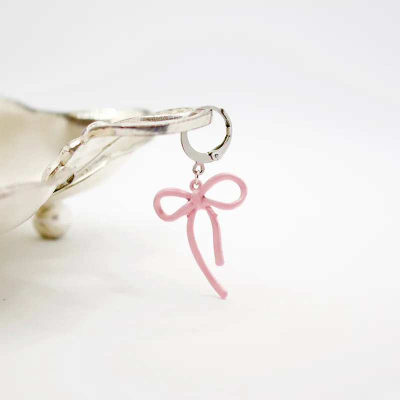 Pink metal knitting marker in the shape of a bow. It hangs delicately from the edge of a silver dish from the second hand store