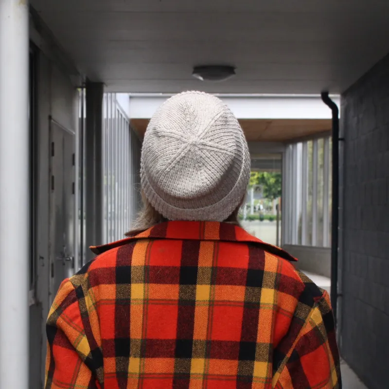 The back view of a woman wearing a grey, hand knit beanie and her father's old swandri jacket.