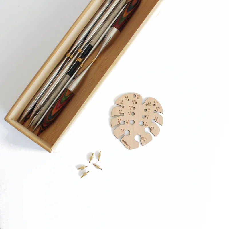 Interchangeable needle tips in a bamboo box with a monstera shaped needle gauge and some joiners
