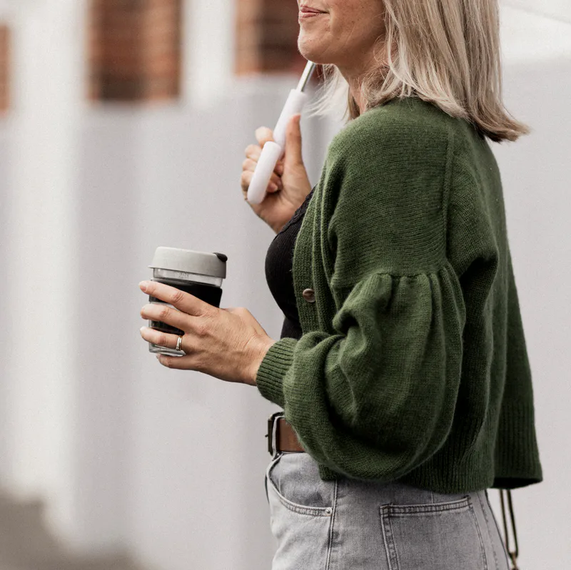 A woman holding an umbrella wearing a green, unbuttoned, hand-knit cardigan