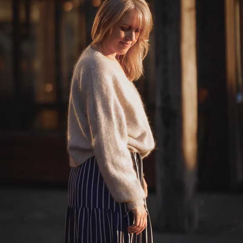 A woman wearing a beige sweater looks down at the ground. The sleeve features a seamless line from the neckline to the cuff and this ridge is the focus of the image