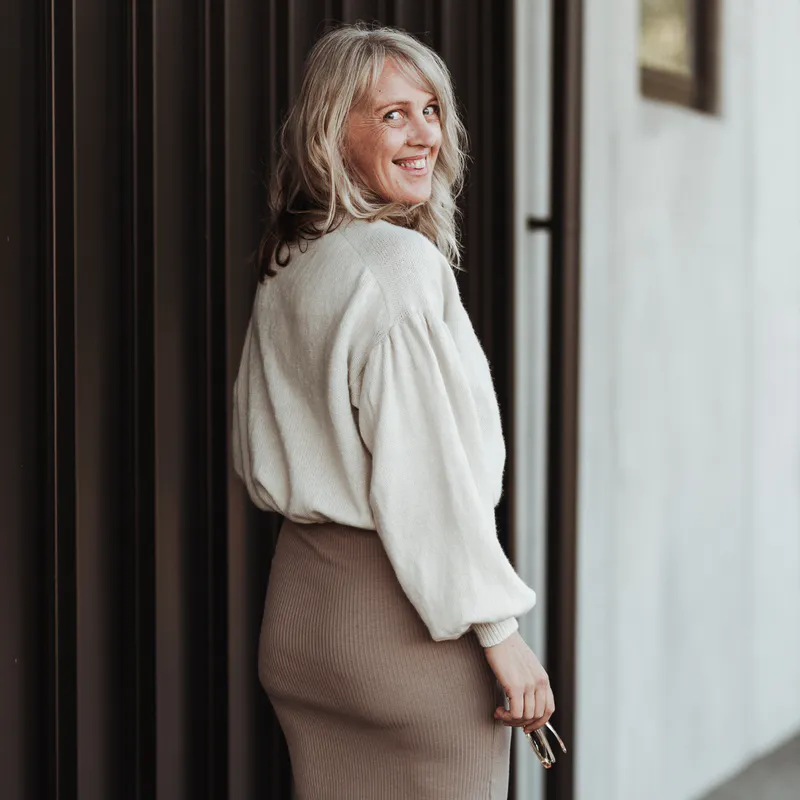 Woman looking over her right shoulder and displaying the back view of her hand knit sweater with a gathered sleeve