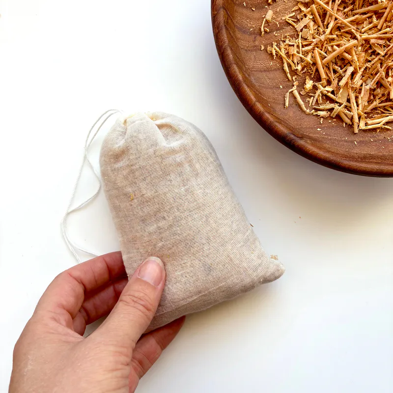 A bag of Himalayan Cedar chips. A hand holds the left bottom corner and a bowl of cedar chips is on the right top corner.