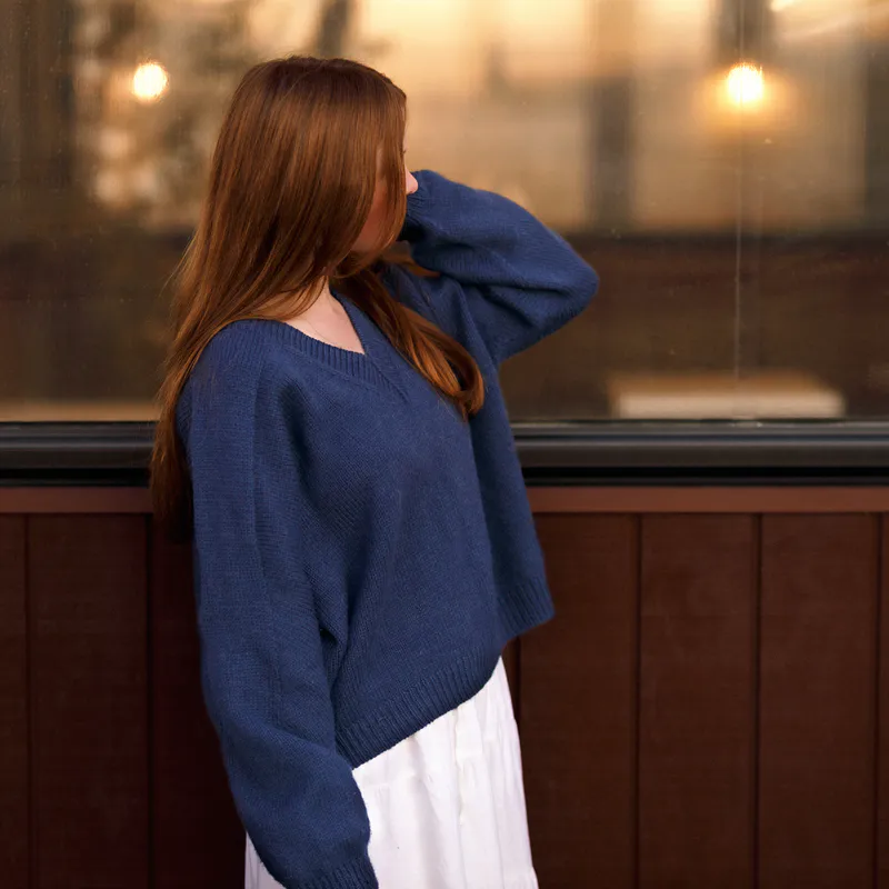 A woman looks away from the camera and the focus is on the sleeve of her navy blue sweater.