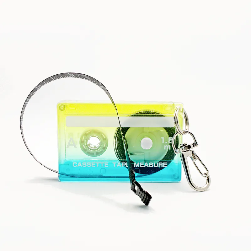 A tape measure in the shape of an 80s cassette tape. It's an ombre colour from blue at the bottom to greenish yellow at the top.