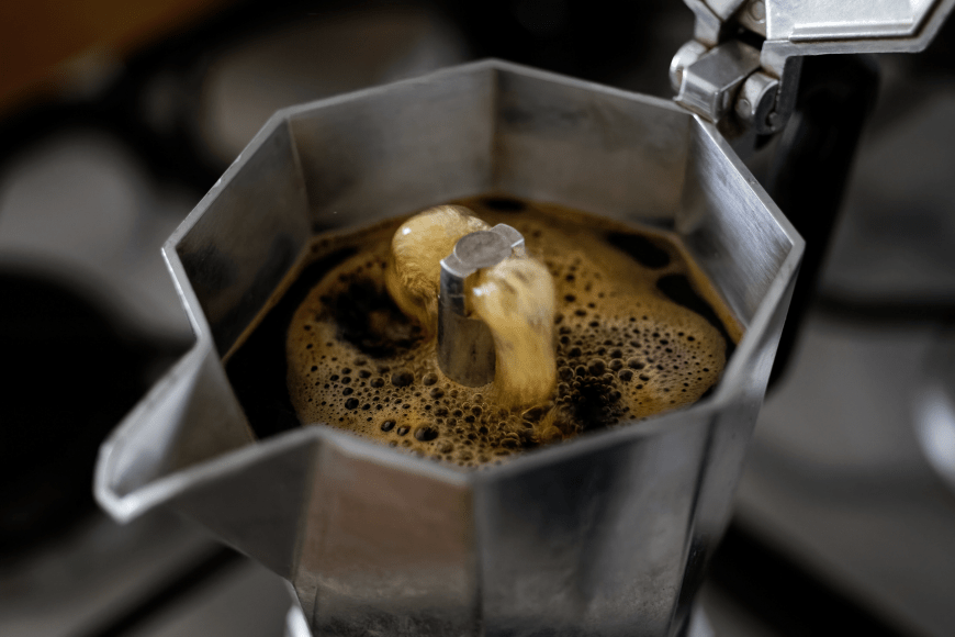 Close up image of coffee brewing in the top chamber of a Bialetti moka pot stovetop coffee maker. The freshly brewing coffee is pouring out of the valve in the centre of the brew chamber