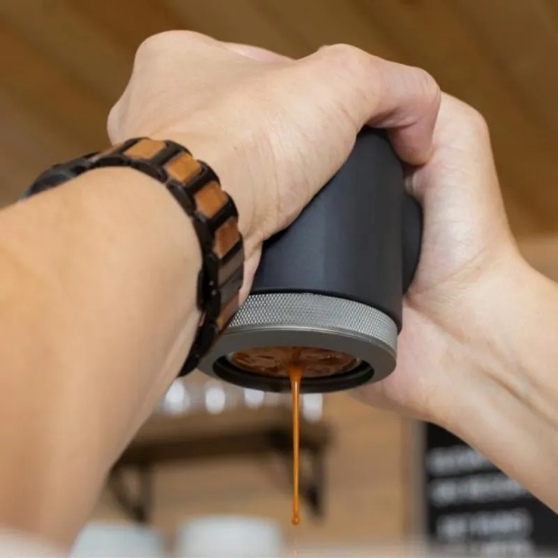 Two hands holding the Picopresso during brewing. Freshly brewed coffee is coming from the naked portafilter.