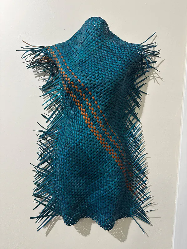 A hand-woven figure of a woman made with dyed Harakeke by Bernie Ross, available at The Little Gallery Whangamatā