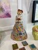 A handmade ceramic sculpture of a lady holding flowers wearing a patchwork dress by Mandy Olsen, available at The Little Gallery Tairua